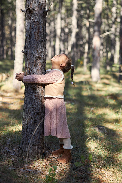 Young girl embracing a tree trunk, enjoying nature in a peaceful forest