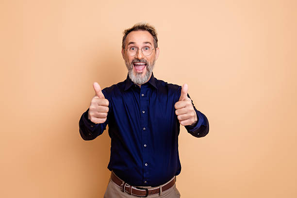 istock Cheerful mature man in formal attire giving thumbs up on a solid beige background 2237093879