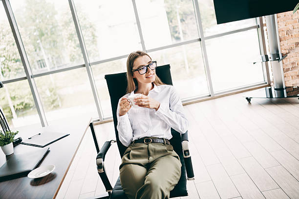 istock Young professional businesswoman relaxing with coffee in a modern office workspace featuring bright windows and a formal attire style 2237094769