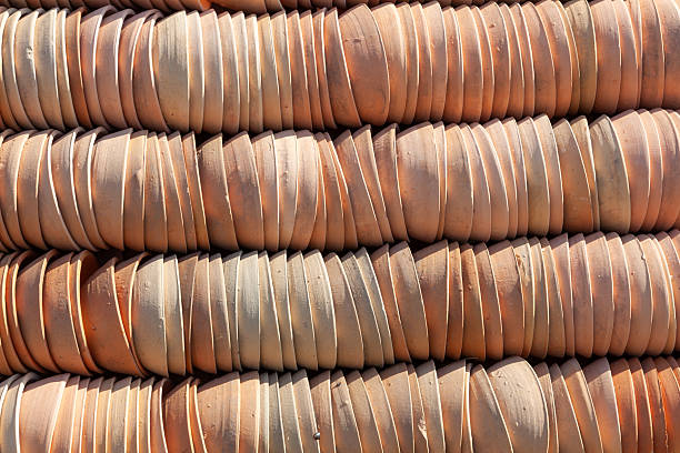 The pottery workshop is a landscape of warm, terracotta hues. Towers of unglazed, yellow clay flower pots are stacked long, their rims creating rhythmic, concentric circles. The porous, matte surfaces have a distinctly earthy texture, absorbing the soft light.