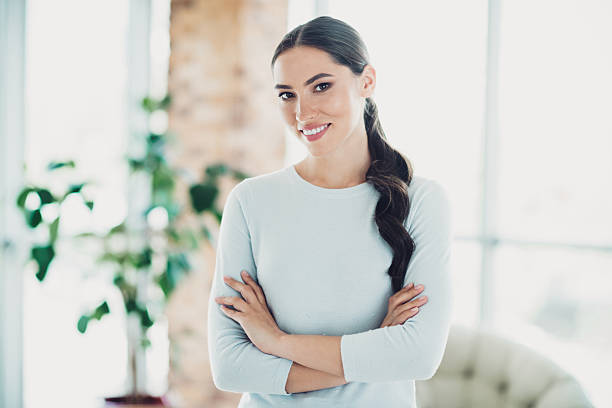 istock Charming young woman with charming smile standing in light modern interior setting with arms crossed and casual attire 2237095358