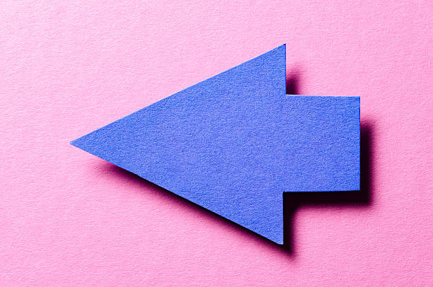 Blue cut out blank paper cardboard arrow direction sign with copy space for text on pink background, flat lay top view pointing symbol conceptual message backdrop