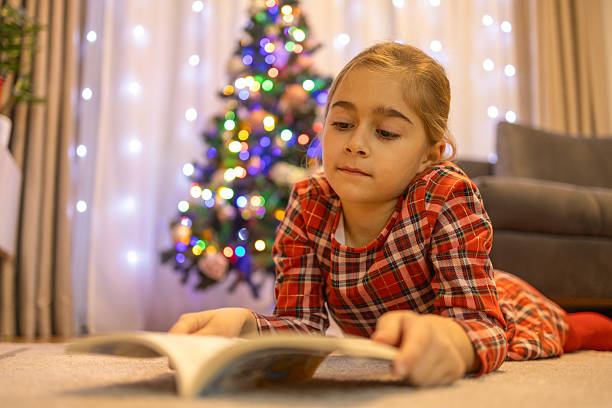 istock Child reading book on floor by christmas tree 2237098682