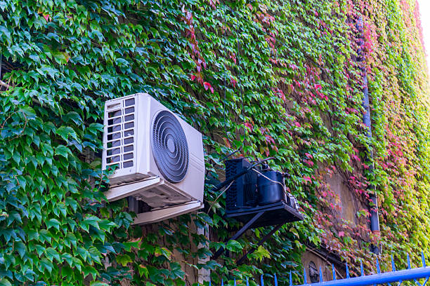 istock Air conditioning units installed on building facade covered with green ivy, contrasting modern technology with natural plant background. 2237104539