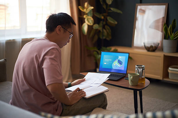 istock Young Adult Asian Man Studying Documents While Using Laptop at Home 2237107966