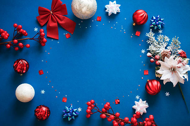Festive Christmas frame with red baubles, snowflakes, berries, frosted pine branches, ribbon bows and confetti, trinkets, and white and red ornaments on dark blue background with copy space in the middle.  Ideal for greeting card mockup. New Year banner template. Christmas and New Year concept.