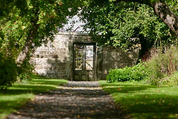 istock A tranquil garden path leads to an old stone wall with a gate, surrounded by lush greenery and dappled sunlight, evoking a peaceful, secret garden atmosphere with rustic charm and natural beauty. 2237131712