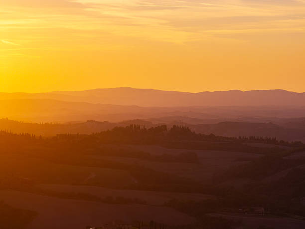Layers of rolling hills and cypress trees receiving warm light during sunset in the Tuscan countryside