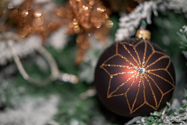 Angled asymmetric shot of cute three dimensional 3D Christmas ornaments shiny red and star shape, golden ball sphere bauble and one jingle bell hanging with thumbtack pin by golden thread, string over fur snow like gray white background bulletin board with copy space for celebration greeting cards, posters, backdrops.