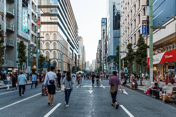 Tokyo, Japan - August 3, 2024: A bustling street scene in Tokyo Ginza district, showcasing pedestrians crossing the road amidst high-end shops and modern architecture..