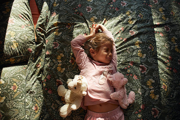 Preschool girl relaxing in sunlight with stuffed animals on floral bedspread