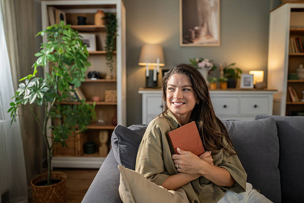 Woman relaxing at home, holding book, smiling