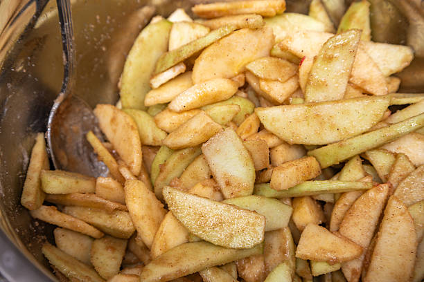 Close-up bowl of mixing spoon stirring raw apple pie filling -- sliced apples, lemon juice, cinnamon, nutmeg, allspice, brown sugar, flour.