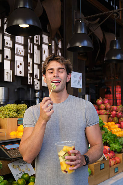Young man eating fresh fruit skewer at market