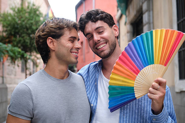 Happy male couple posing together, showing love and support with a colorful pride fan