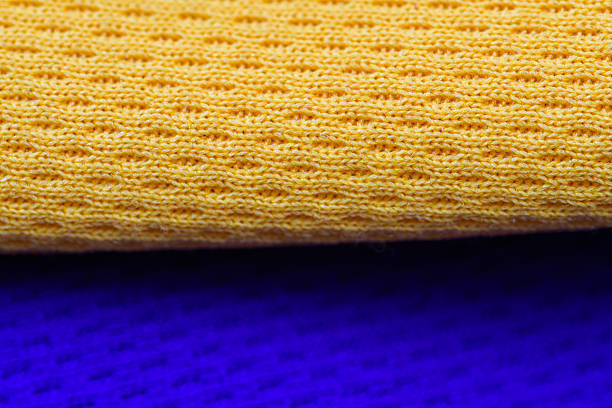 This macro shot captures the intricate texture of yellow knitted fabric contrasted against a vibrant blue background. The close-up perspective highlights the pattern and structure of the knit, creating a visually engaging abstract image. The bright yellow and blue colors offer a striking contrast suitable for various design applications.