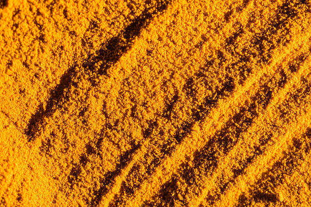 This macro photograph showcases the detailed texture of vibrant yellow turmeric powder, highlighting its fine granules and natural variations in color. The composition emphasizes the rich, warm tones and creates an abstract, organic feel, suitable for culinary or wellness concepts.