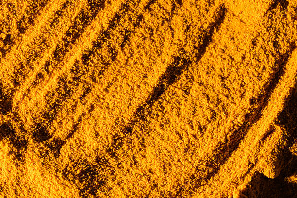 Close-up photograph capturing the vibrant texture of turmeric powder, showcasing its rich yellow-orange hue and granular consistency. The image highlights the surface details and patterns created by the spice, ideal for illustrating concepts related to cooking, health, spices, and natural remedies.