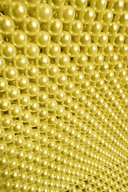 Close-up of shiny golden beads arranged in a dense, repeating pattern, creating a textured and luxurious surface with reflective highlights.