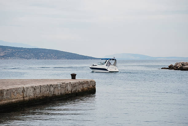 Krk, Croatia - August 30, 2012 - Motorboat navigating calm waters near rocky shoreline under cloudy sky.