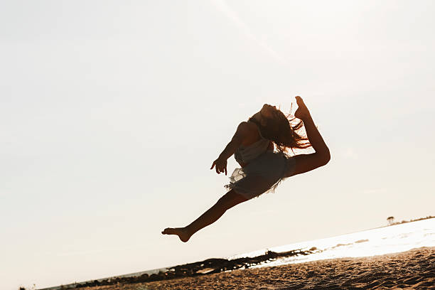 Pretty woman in jeans leaping on the beach in winter