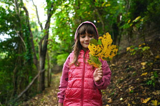 Child enjoying nature and holding a colorful leaf in the woods