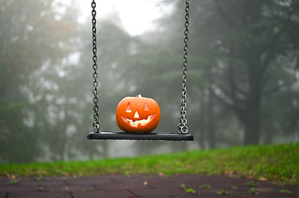 istock Jack-o'-lantern sitting on a swing in foggy park 2237186450