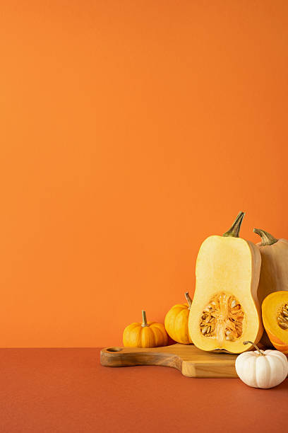 Side vertical view of squash and pumpkins arranged on a cutting board with orange background, evoking fall vibes, Thanksgiving traditions, and the harvest season