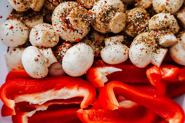Bright red bell peppers and white mushrooms are seasoned and prepared for a delicious meal. The vibrant colors highlight the freshness of the ingredients creating an appetizing scene.