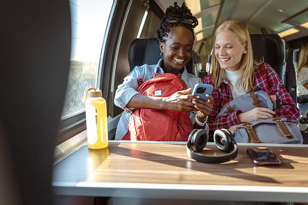 istock Two friends on a train enjoying a sunny journey while looking at a smartphone together 2237189342