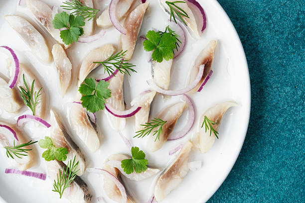 istock Marinated herring slices with red onion and herbs on white plate with napkin over blue background 2237211882
