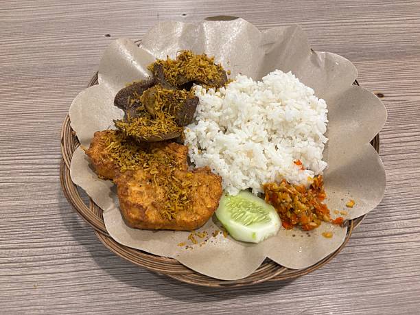 istock Authentic nasi empal served with fried beef, chicken, sambal, cucumber, and white rice on a woven plate lined with brown paper. 2237232003