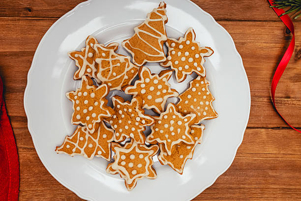 A white plate filled with decorated gingerbread cookies in festive shapes is placed on a wooden table