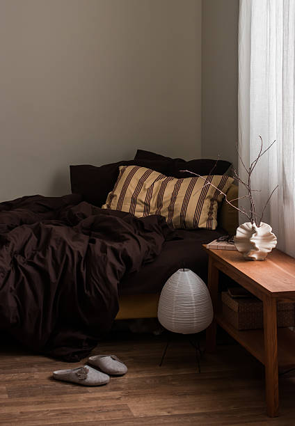 istock Cozy bedroom interior - a disassembled bed with brown linens, a bench with decor, a lamp 2237243505