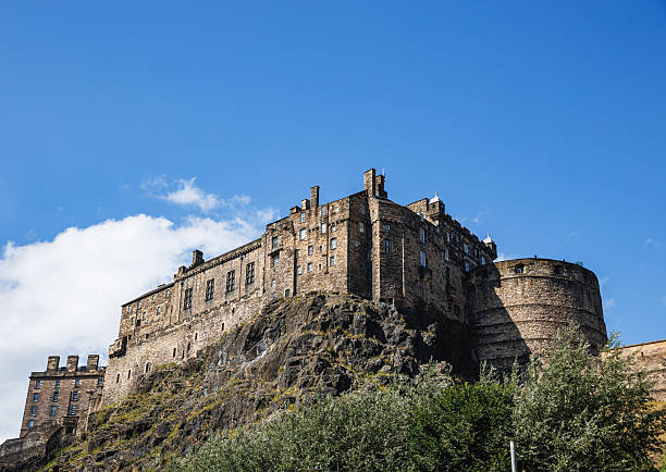 Majestic Edinburgh Castle perches on rugged rock, stone walls rising above lush greenery. A timeless Scottish fortress bathed in sunlight, conveying history, strength, and culture—perfect for editorial travel, heritage, and tourism themes.