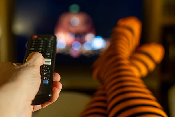 istock Relaxing Halloween streaming indoors with striped socks, remote control in hand, blurred television screen and cozy autumn lifestyle vibes. 2237249362