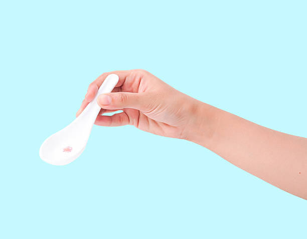 istock Hand holding white ceramic spoon with a small amount on light blue background. 2237252262