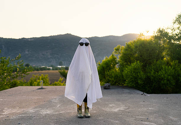 Child in a White Ghost Costume Standing Outdoors at Sunset