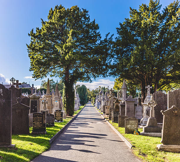 A small path through a cemetery with tombstones and grave stones with crosses under a cloudy sky.