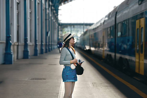 A traveler wearing a hat photographs a departing train on an outdoor platform, capturing the energy of a bustling station.