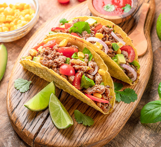 Mexican meat tacos or beef stuffed tortillas and lime slices near them on wooden serving board.