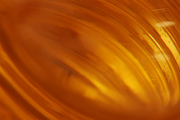 This image captures the captivating effect of light interacting with a textured glass surface. The glass's uneven, bumpy texture creates a diverse array of shadows and highlights, resulting in a visually striking pattern. The gradient of light, transitioning from a darker hue at the top to a warm, amber glow at the bottom, accentuates the depth and contours of the glass's surface. The play of light and shadow on the glass's texture generates an abstract, almost ethereal quality, turning a common material into a canvas for light. This photograph serves as a testament to the beauty found in the interplay between light and physical textures, highlighting how even transparent materials can reveal intricate details when viewed from a different perspective.