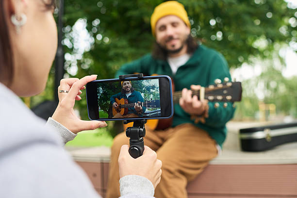 Young Caucasian Man Playing Guitar Outdoors While Woman Recording Video