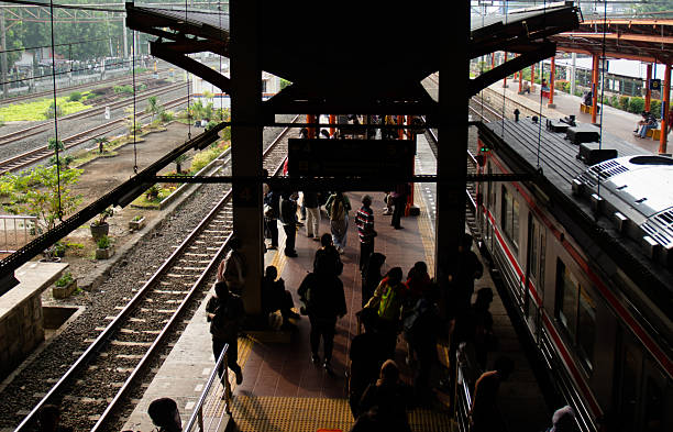 A group of passengers stands on a station platform while waiting for the arrival of a commuter train. The image highlights the daily routine of urban transportation, showcasing people in casual and formal attire ready for their journey. Suitable for concepts of public transport, city lifestyle, and commuting culture in modern metropolitan areas.