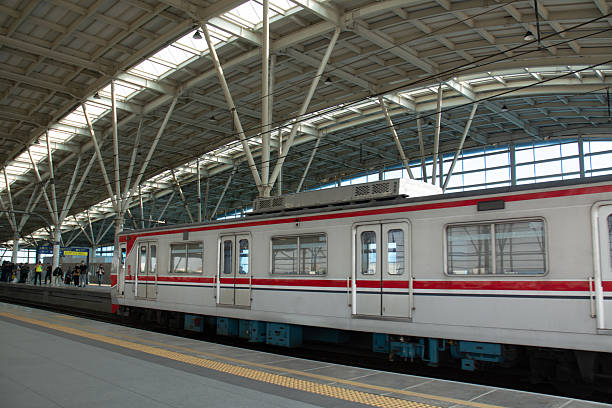 A group of passengers stands on a station platform while waiting for the arrival of a commuter train. The image highlights the daily routine of urban transportation, showcasing people in casual and formal attire ready for their journey. Suitable for concepts of public transport, city lifestyle, and commuting culture in modern metropolitan areas.