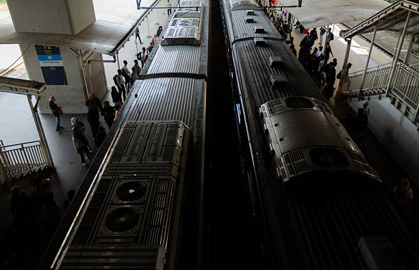 A group of passengers stands on a station platform while waiting for the arrival of a commuter train. The image highlights the daily routine of urban transportation, showcasing people in casual and formal attire ready for their journey. Suitable for concepts of public transport, city lifestyle, and commuting culture in modern metropolitan areas.