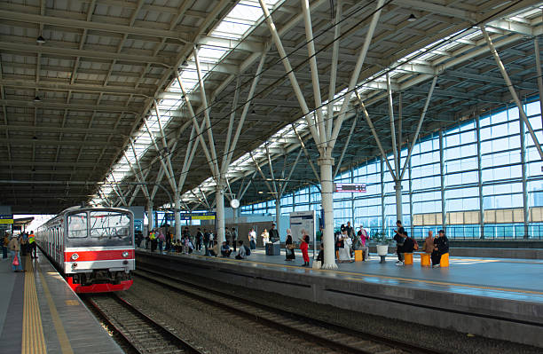 A group of passengers stands on a station platform while waiting for the arrival of a commuter train. The image highlights the daily routine of urban transportation, showcasing people in casual and formal attire ready for their journey. Suitable for concepts of public transport, city lifestyle, and commuting culture in modern metropolitan areas.