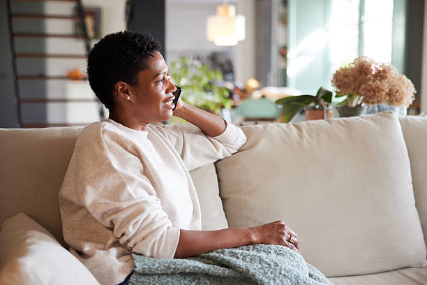 istock A woman smiles while talking on the phone, relaxed and comfortable on the sofa. 2237280944