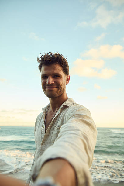 istock Man at the beach taking a selfie during sunset with ocean waves in the background 2237281387