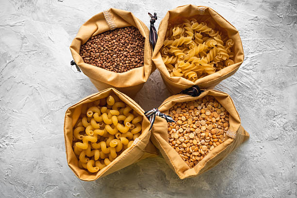 Three glass bowls filled with green, orange, and brown lentils sit on a dark countertop. Each bowl has a small wooden scoop for easy serving, highlighting nutritious ingredients for cooking - food and drink, food allergies